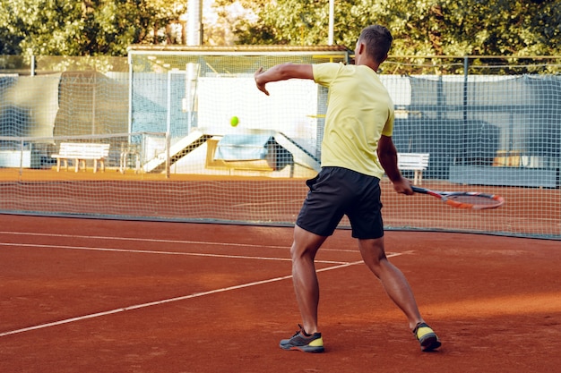 Back view of a man playing tennis on tennis court