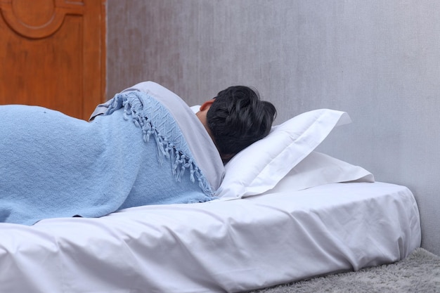 毛布を持って寝室で寝ている男性の背面図