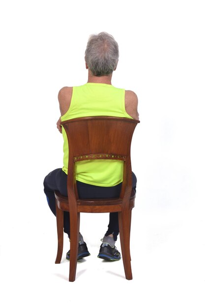 Back view of a man in sportswear tights and fluorescent yellow sleeveless sitting on chair arms crossed on white background