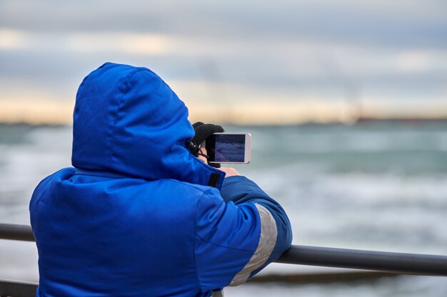 Back view of man tourist taking photo of seascape with smartphone