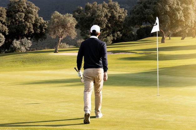 Vista posteriore dell'uomo che cammina verso la bandiera sul campo da golf