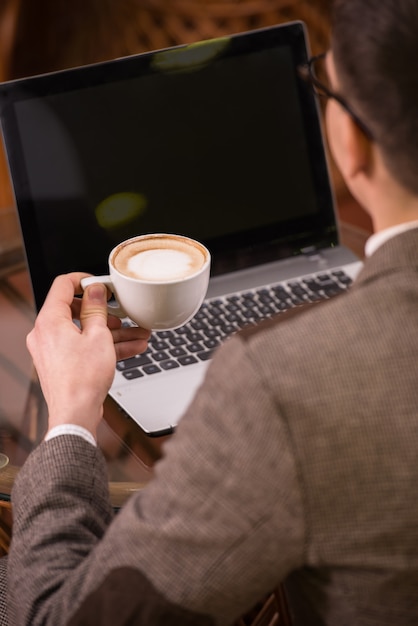 Back view of man with laptop and coffee at cafe.