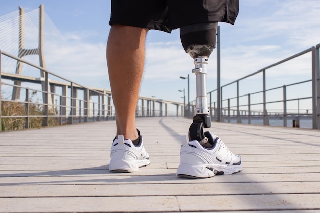 Back view of man with mechanical leg on summer day. Sportsman in black shorts and white sneakers photographed during training. Sport, disability, hobby concept