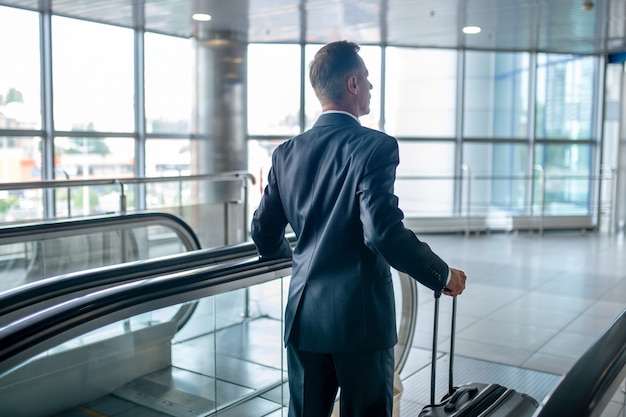 Back view of man with suitcase on escalator