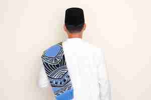 Photo back view of moslem man standing with prayer mat on his shoulder