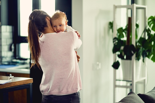 Back view of mother enjoying while holding her baby at home