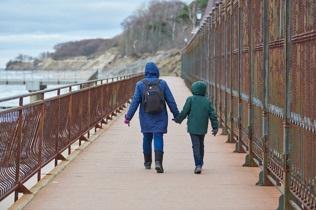 冬の海の近くの岸壁に沿って歩く母と息子の背面図