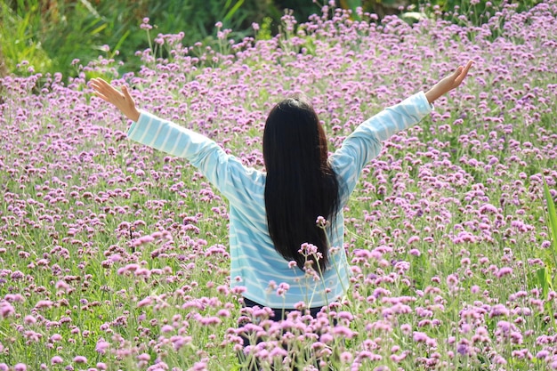사진 아시아의 긴 머리카락을 가진 여성이 작은 보라색 꽃을 배경으로 손을 들어 올립니다.