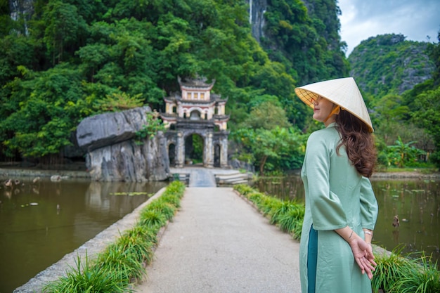 사진 아오다이 (ao dai) 를 입은 소녀의 뒷모습, 호수와 돌교가 있는 야외 공원 풍경, 고대 비치돈 (bich dong) 파고다 복합 건물의 입구, 닌빈 (ninh binh) 베트남 여행지