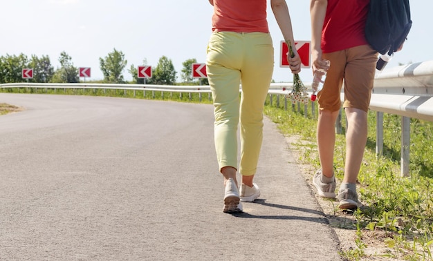 写真 道路に沿って一緒に歩くスリムな女性と男性の足の背面図旅行とハイキングのコンセプト