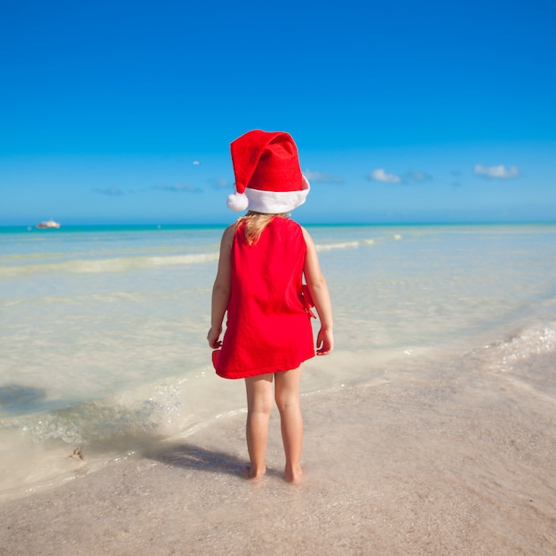 ビーチで赤い帽子サンタクロースでかわいい女の子の背面図