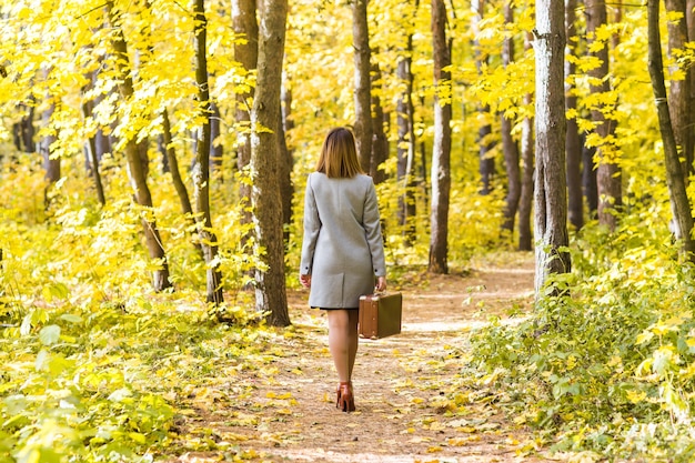 가을 공원에서 산책하는 복고풍 가방을 가진 젊은 세련된 여자의 뒷면