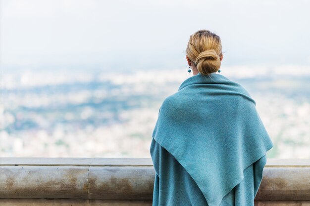 Foto vista posteriore della giovane donna solitaria pensierosa in vestiti blu che esamina la distanza con speranza.