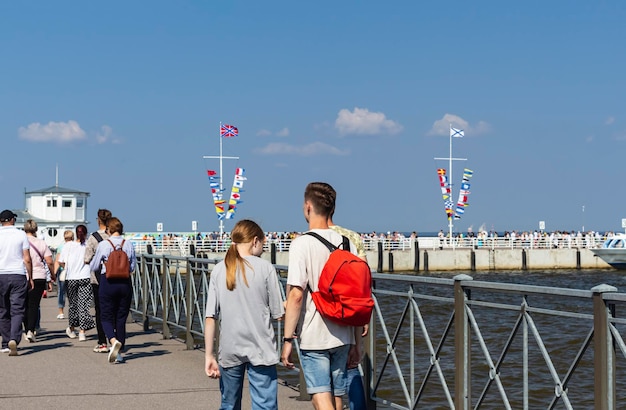 晴れた夏の日に海で桟橋旅客輸送に沿って歩く人々 の背面図