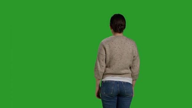 Photo back view of person showing denial and pushing something aside, expressing refusal and rejection looking displeased. female model acting discontent and moving object, standing over greenscreen.