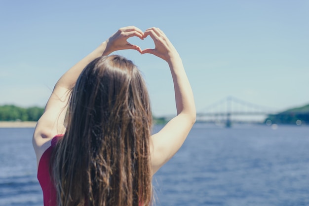 Back view photo of girl gesturing heart nature river background