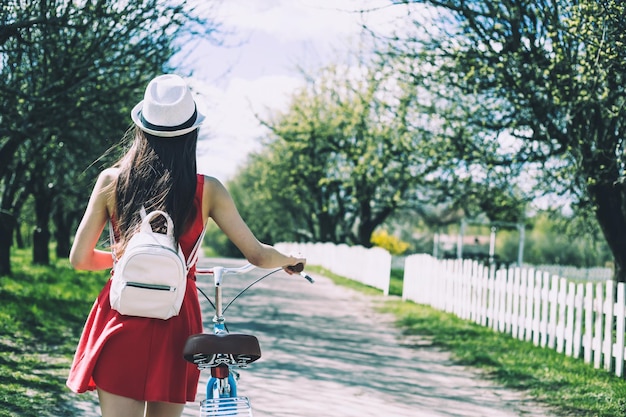 Back view photo of young woman with blue bicycle outdoors