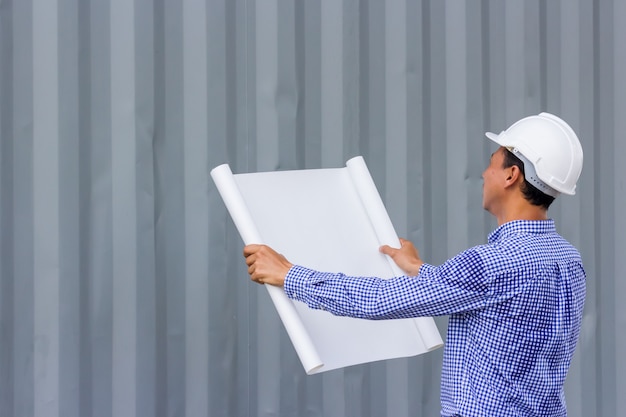 Back view portrait of Asian engineer holding plans against wall while standing on construction site, copy space
