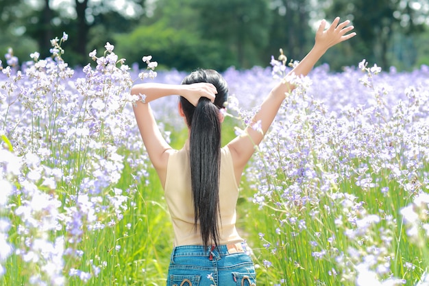 Back view portrait of beautiful woman having a happy time and enjoying among flower naga-crested field in nature