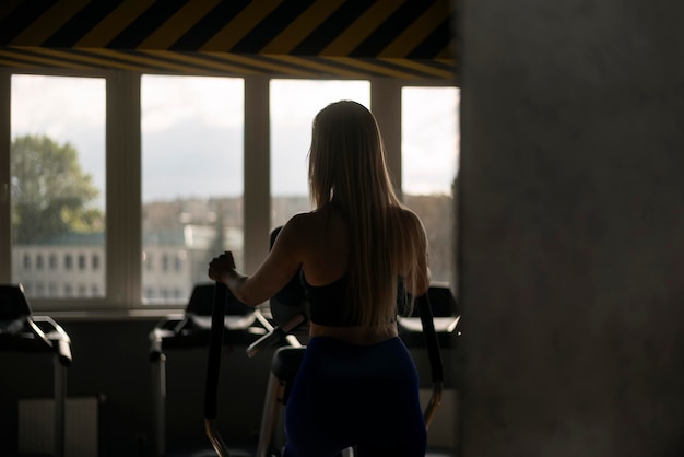 Back view portrait of girl with long hair in the gym training on the orbitrek Elliptical Trainer