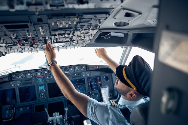 Back view portrait of male wearing uniform pushing buttons in cockpit during flight