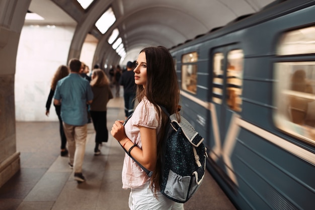 写真 地下鉄で電車を待っているバックパックを持つ少女の背面図の肖像画。