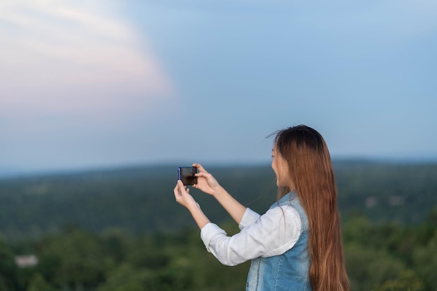 スマートフォンで風景の写真を撮る女性の背面図の肖像画