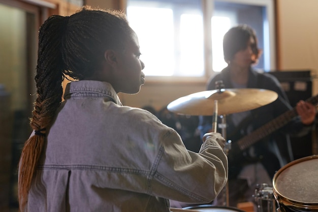 Back view portrait of young female drummer playing music with\
band during rehearsal in studio copy s