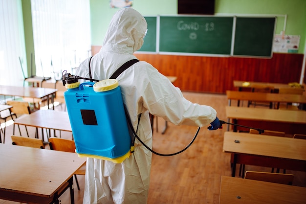 Vista posteriore di un operatore sanitario professionista che disinfetta l'aula prima dell'inizio dell'anno accademico. un uomo che indossa una tuta protettiva pulisce l'auditorium dal coronavirus covid-19. assistenza sanitaria.