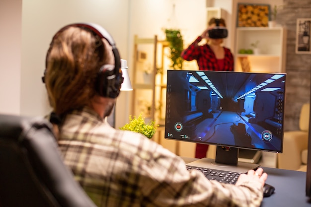 Photo back view of professional video gamer playing on powerful pc late at night in the living room.