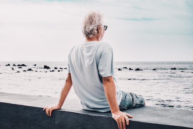 Back view of relaxed senior man sitting face the sea at sunrise looking at horizon enjoying freedom and retirement