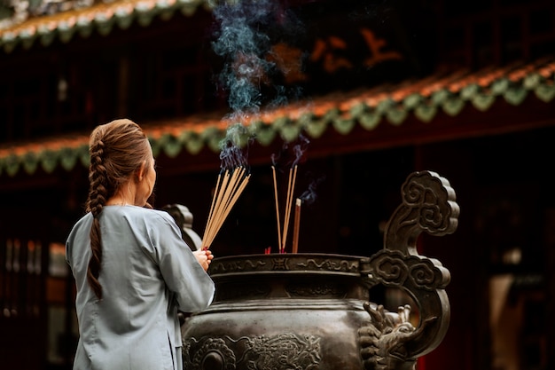 Foto vista posteriore della donna religiosa al tempio con incenso ardente