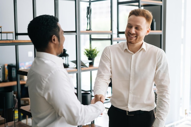 back view of satisfied caucasian boss shake hand of african american partner in modern office boardroom
