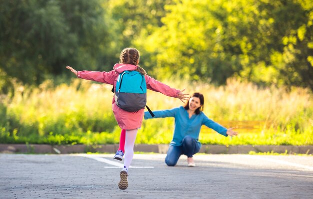 back view of school girl running to mother after class on sunny street