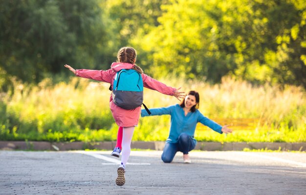 Back view of school girl running to mother after class on sunny street