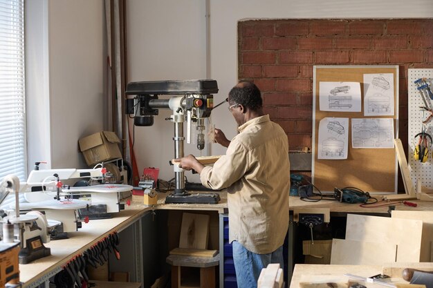 Back view of senior black man cutting wood using machines in workshop