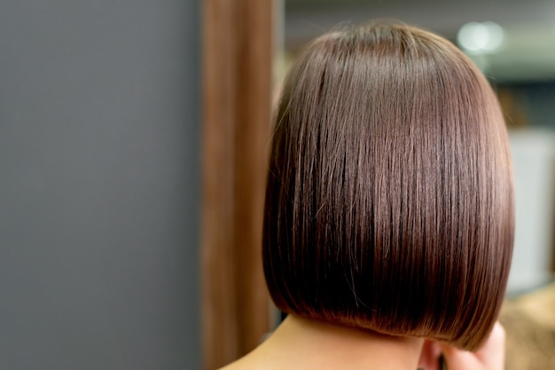 Back view of short hairstyle of woman looking in the mirror in hair salon