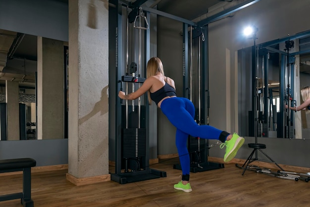 Back view on a slender woman in the gym doing exercises for the legs and buttocks Beautiful sportive young woman