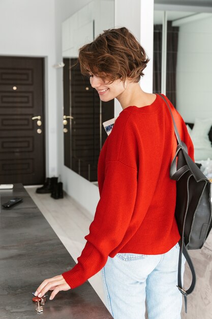 Back view of a smiling woman with backpack leaving her apartment