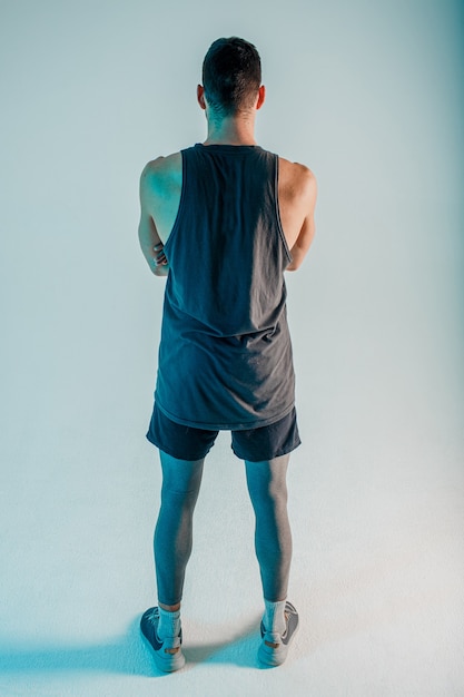 Back view of sportsman with crossed arms. Man wear sports uniform. Isolated on gray background with turquoise light. Studio shoot.
