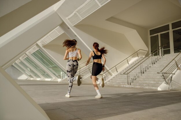 Photo back view of sporty female friends in sportswear running outdoors on a sunny day morning jog