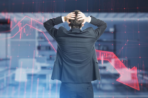 Photo back view of stressed thoughtful businessman with red candlestick arrow going down on blurry office interior background economic recession and crisis concept double exposure