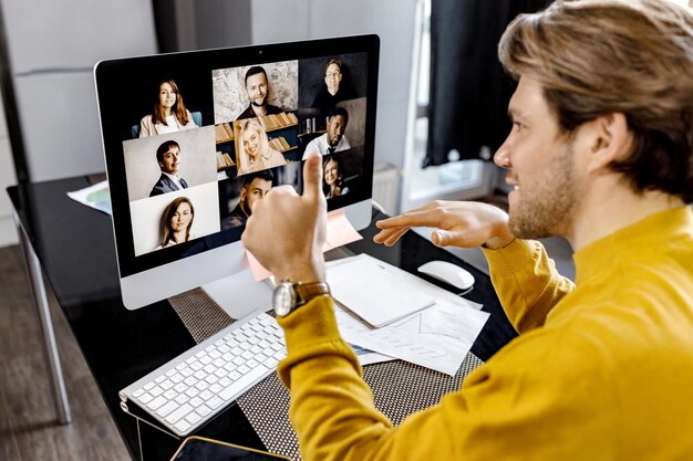 Foto punto di vista posteriore dell'uomo d'affari alla moda in camicia gialla che discute un progetto con i colleghi in video