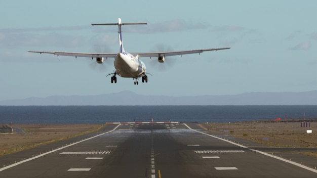 滑走路に着陸する飛行機の成功の背面図。海沿いの空港に到着。熱歪みのあるビュー