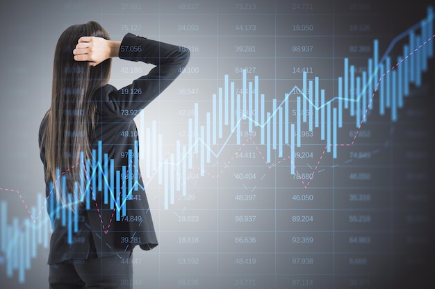 Вид сзади вдумчивой молодой бизнесвумен, смотрящей на светящийся график форекс свечей на сером фоне с индексом Торговля акциями и глобальная финансовая концепция Двойная экспозиция