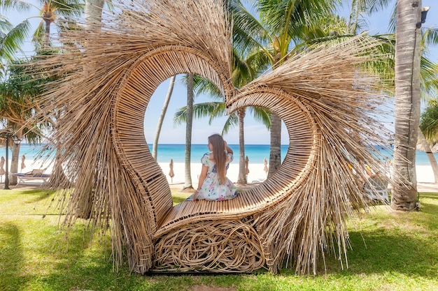 Back view of tourist woman sitting in photo spot like straw heart with palm tree