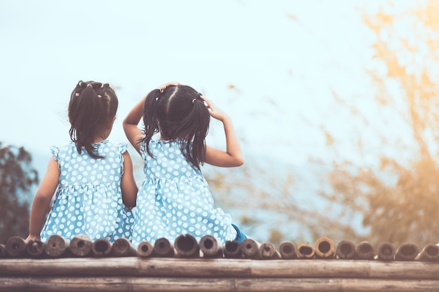 Back view of two child girls sitting and looking at nature together in vintage color tone