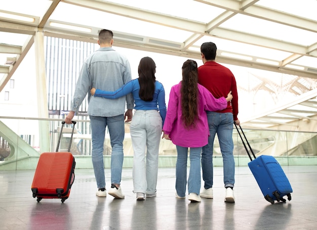 Back view of two couples standing with suitcases in airport