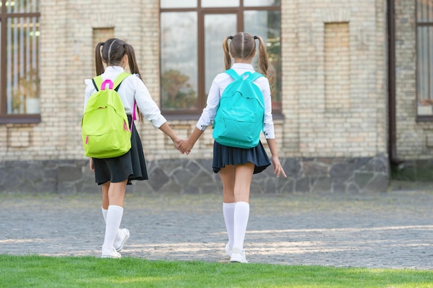 Back view of two schoolgirls with school backpack walking\
together outdoor friendship