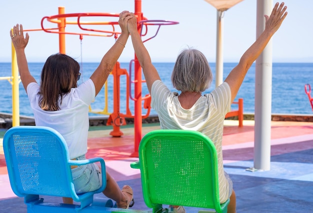 Back View of two Senior Women Have Fun Doing Exercises in Public Open Air Gym Equipment at Sea
